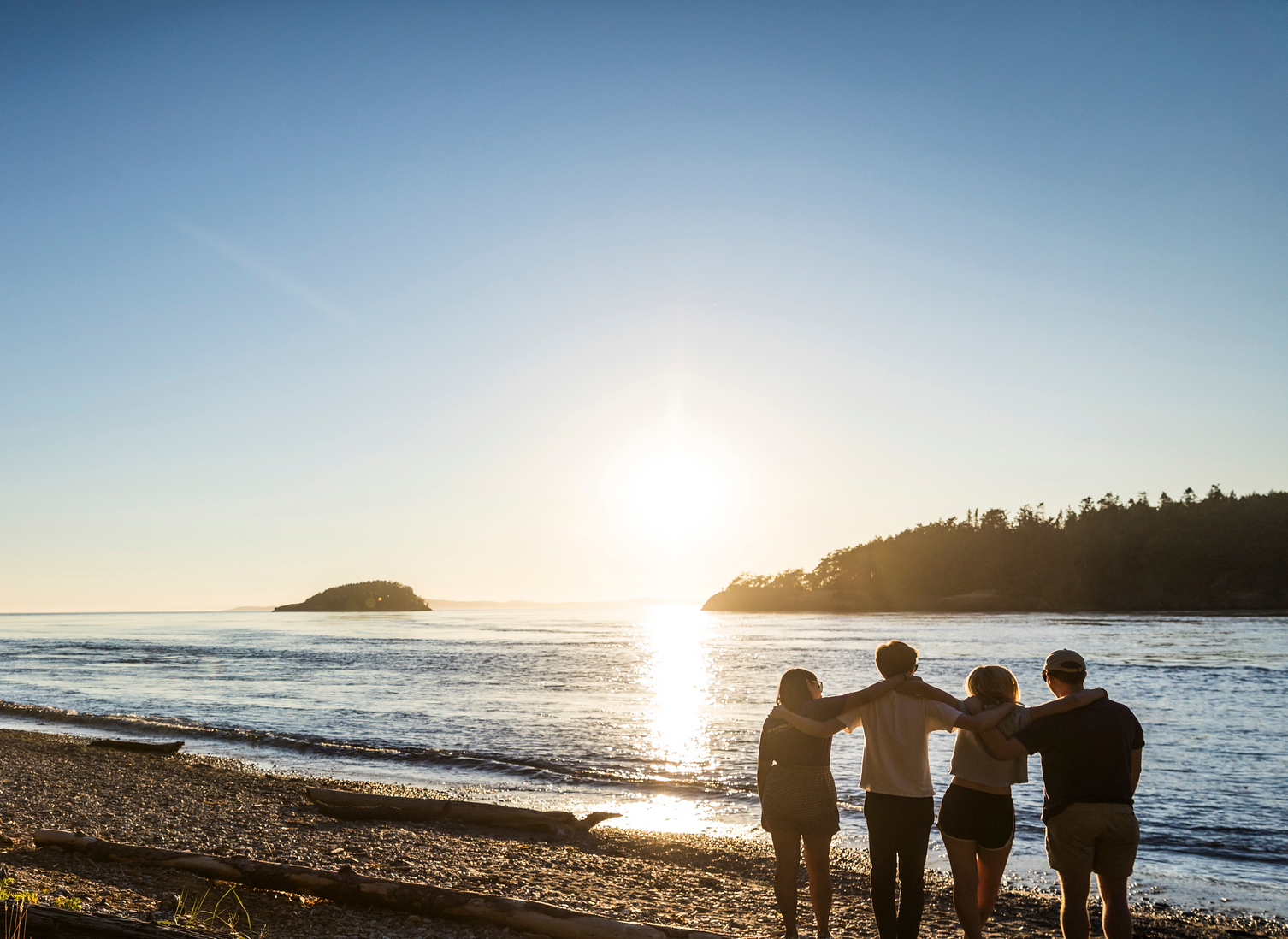 A group of four people stand on the beach at sunset.